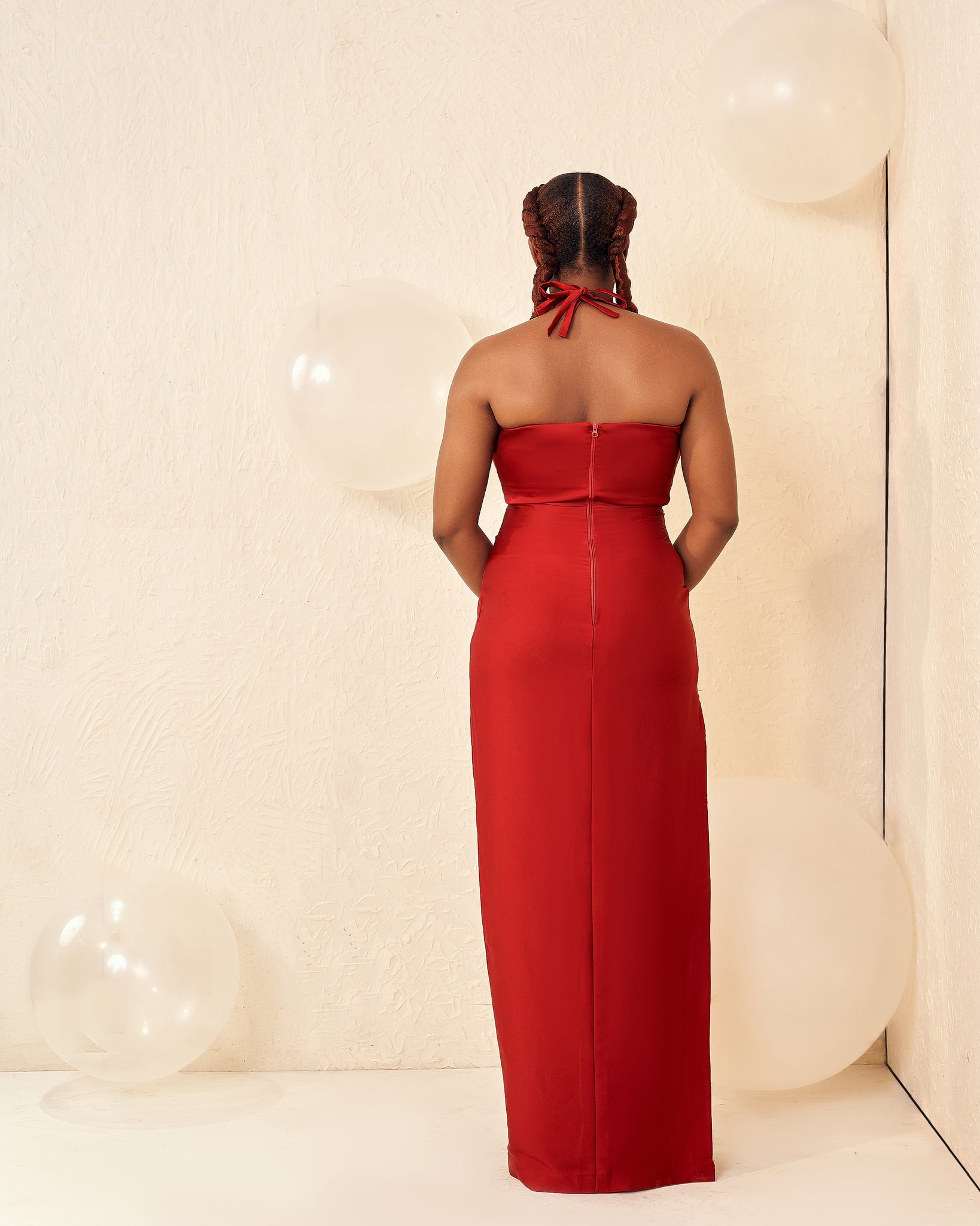 Woman in red halter neck dress standing in minimalist room with white balloons