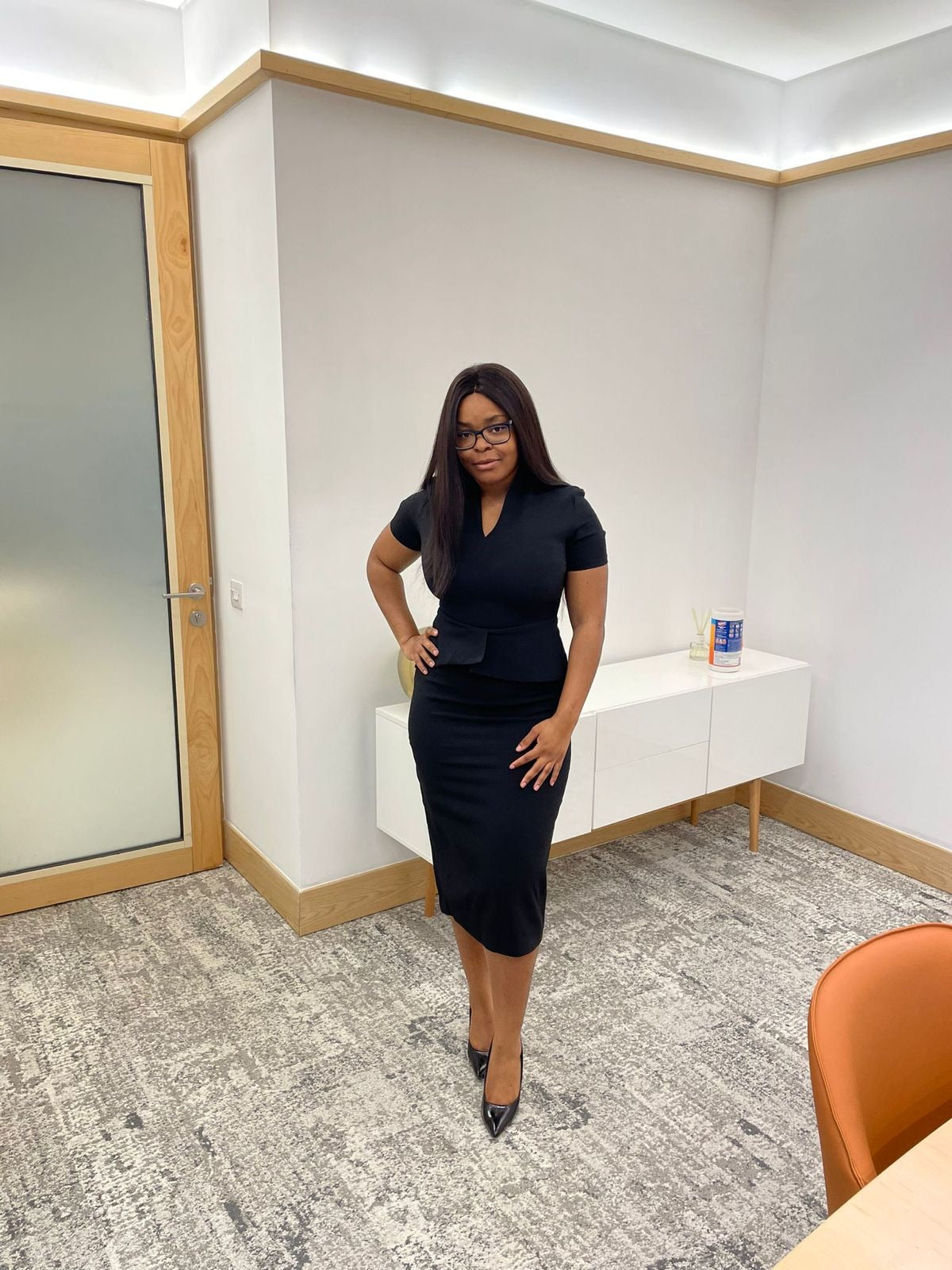 Woman in fitted black dress and heels standing in modern office setting