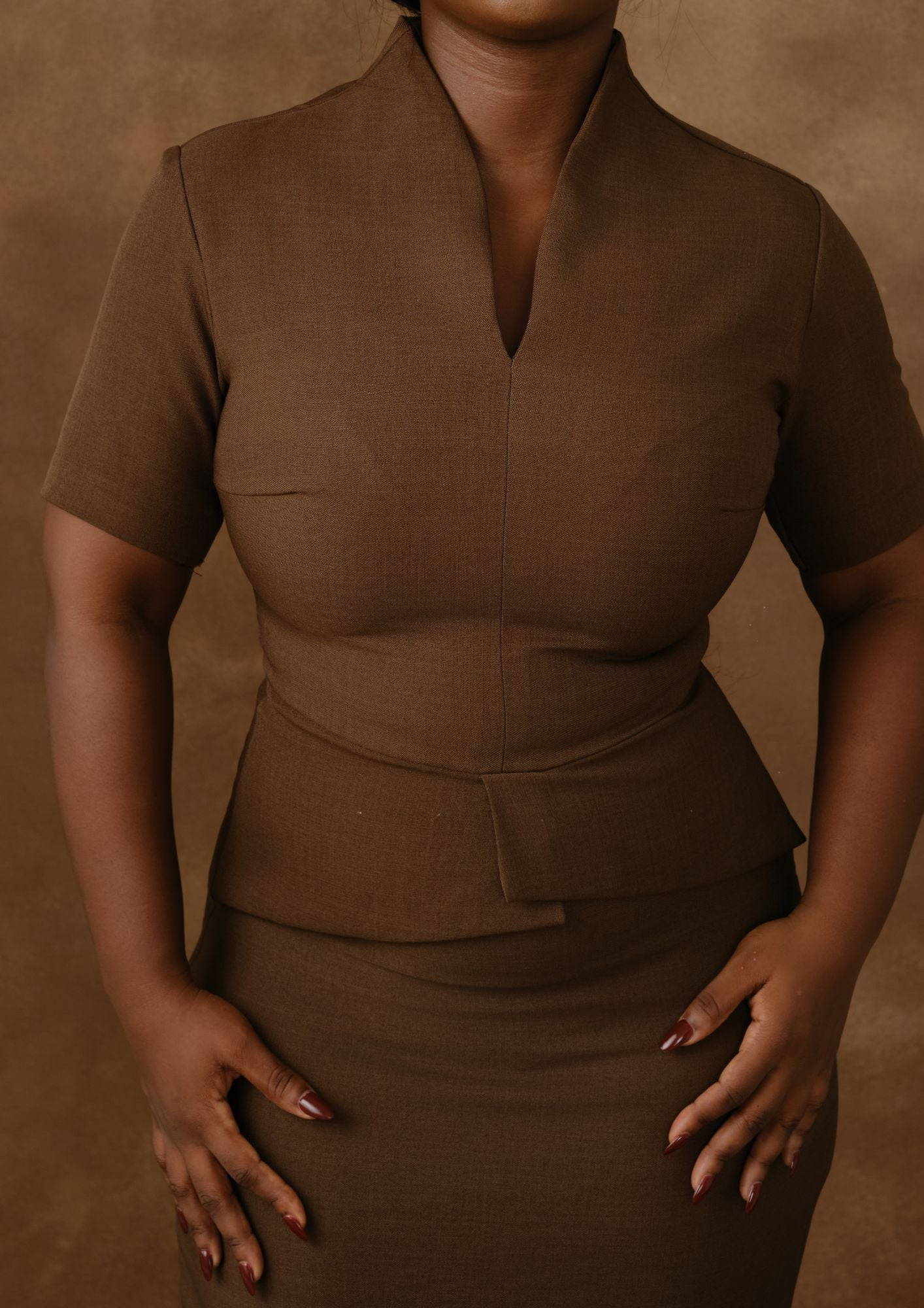 Woman wearing a tailored brown peplum dress with short sleeves, neutral studio background